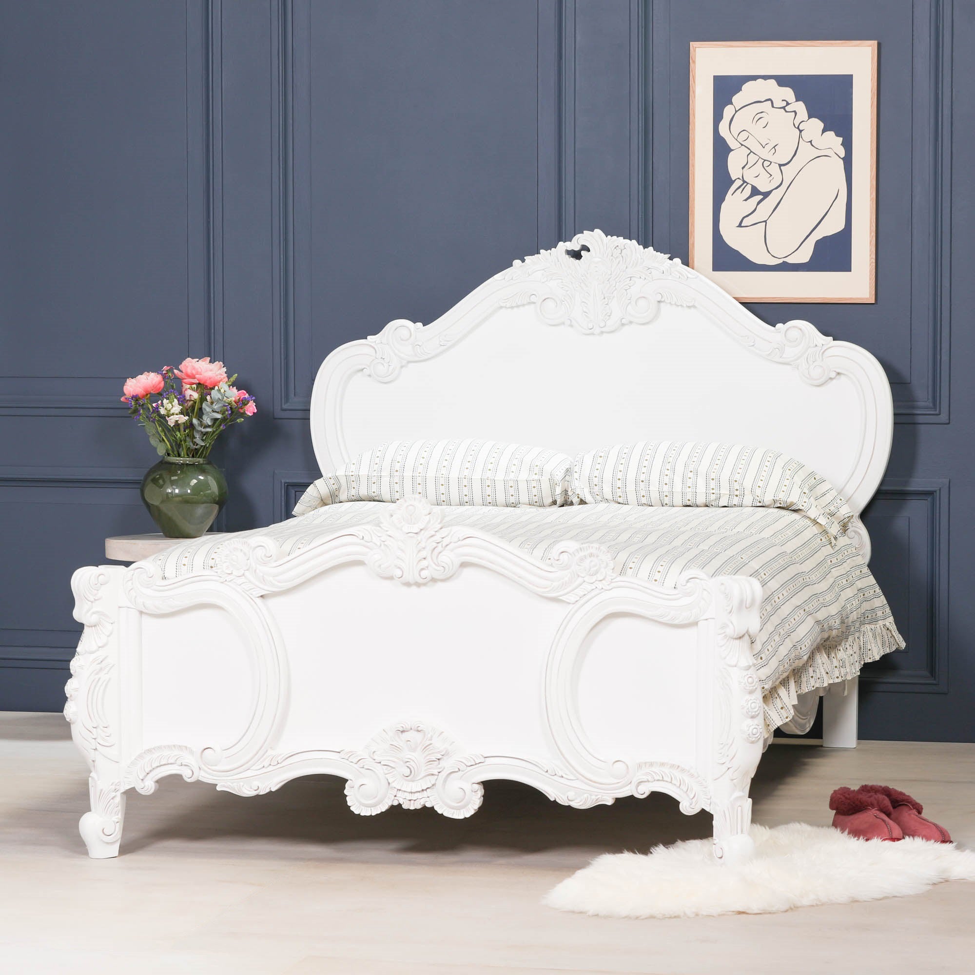 Rosalie French Rococo 4ft6 double bed frame in light painted white with hand-carved rose and cherub detailing, styled in an elegant bedroom with dark blue panelled walls, framed artwork and luxury bedding.