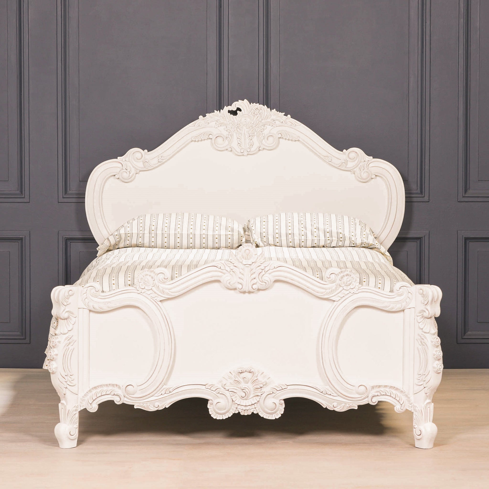 Front view of the Rosalie French Rococo 5FT king size bed against dark wall panelling, highlighting the light painted white finish and elaborate hand-carved rose and cherub detailing