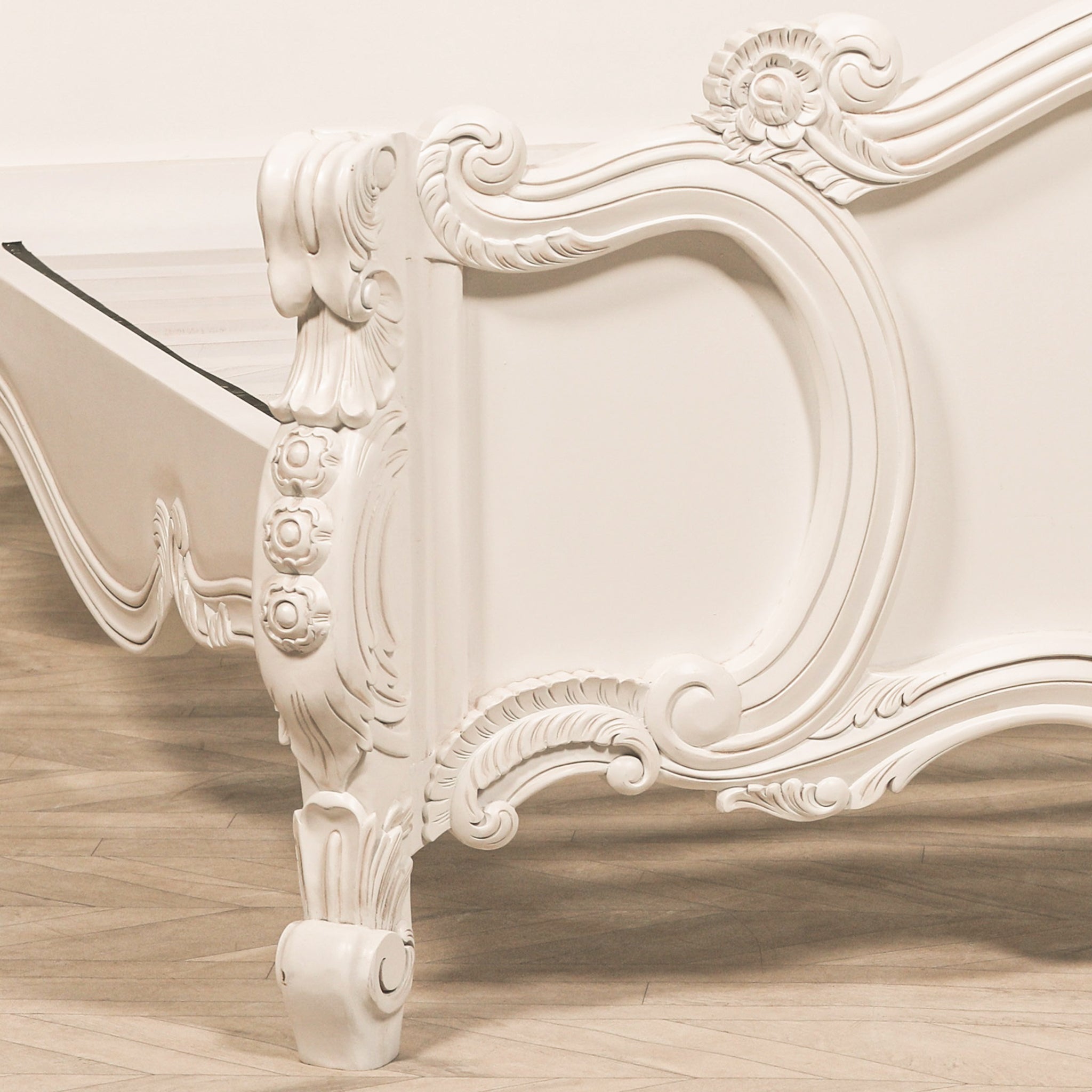 Close-up of the Rosalie French Rococo bed frame footboard corner with ornate hand-carved floral scrollwork, curved moulding and sculpted leg in painted white