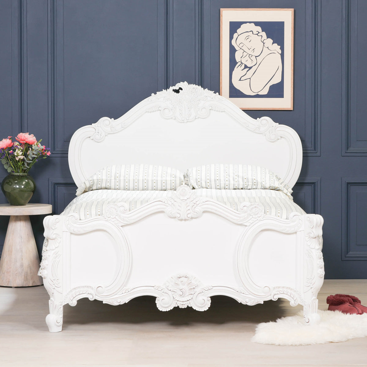Front view of the Rosalie French Rococo double bed frame in light painted white featuring ornate hand-carved rose and cherub detailing against dark blue panelled walls with decorative bedroom styling.