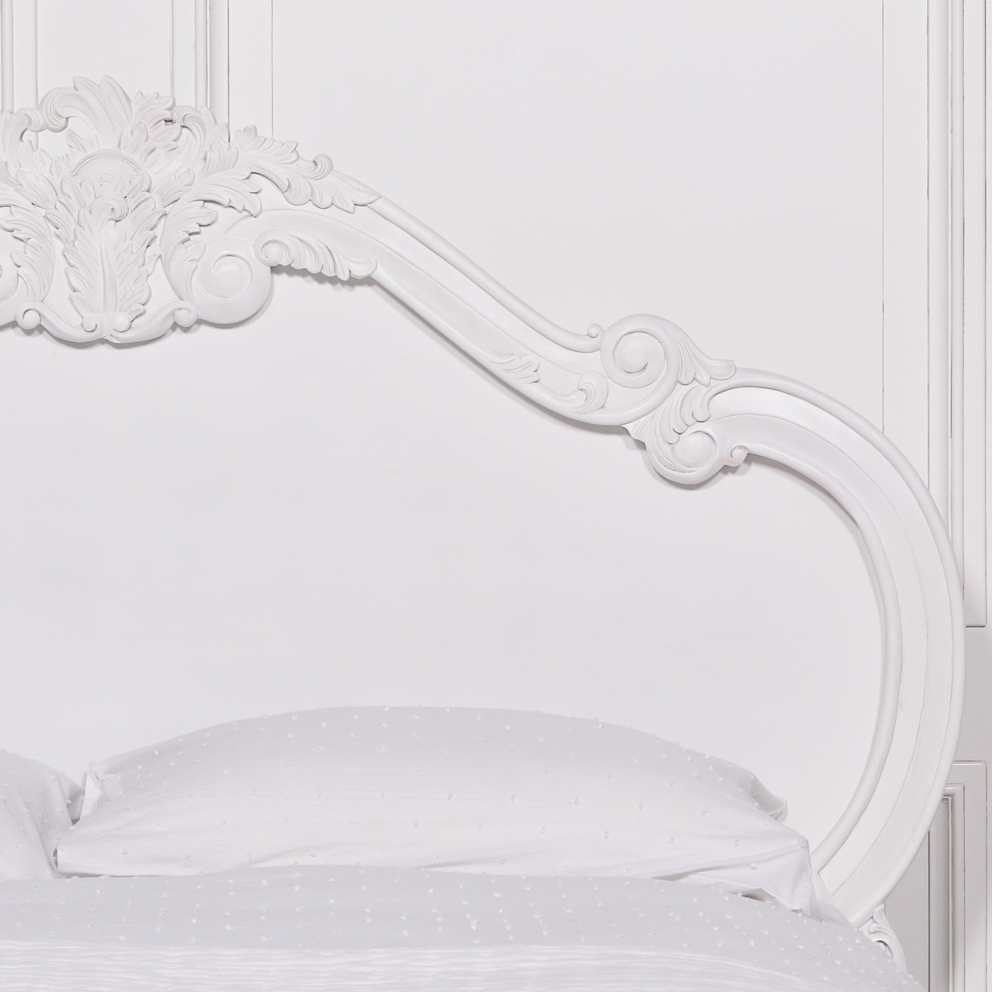 Curved Rosalie French Rococo headboard with intricate hand-carved rose and cherub detailing in a light painted white finish above luxury white bedding.