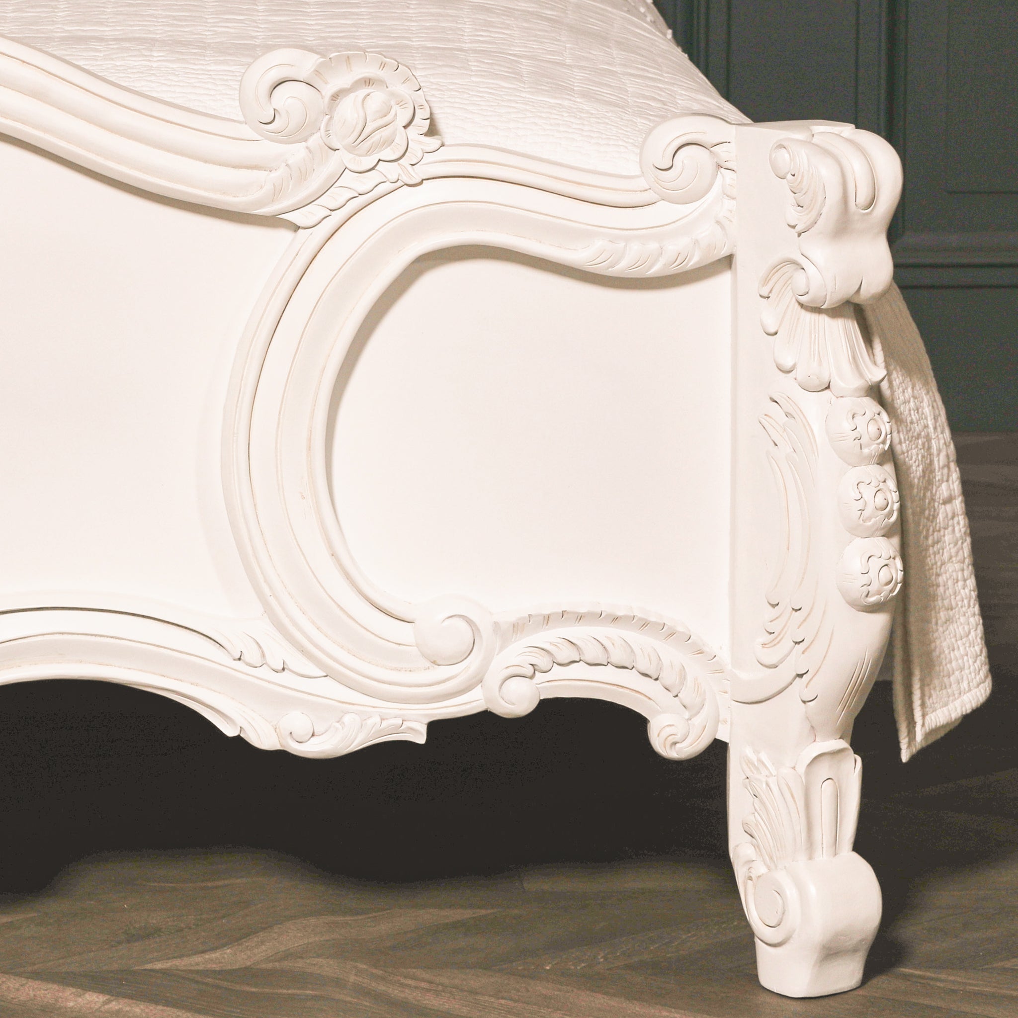 Close-up of the Rosalie hand-carved white Rococo bed footboard showing curved panel moulding, floral rosettes, carved scrollwork and sculpted corner leg
