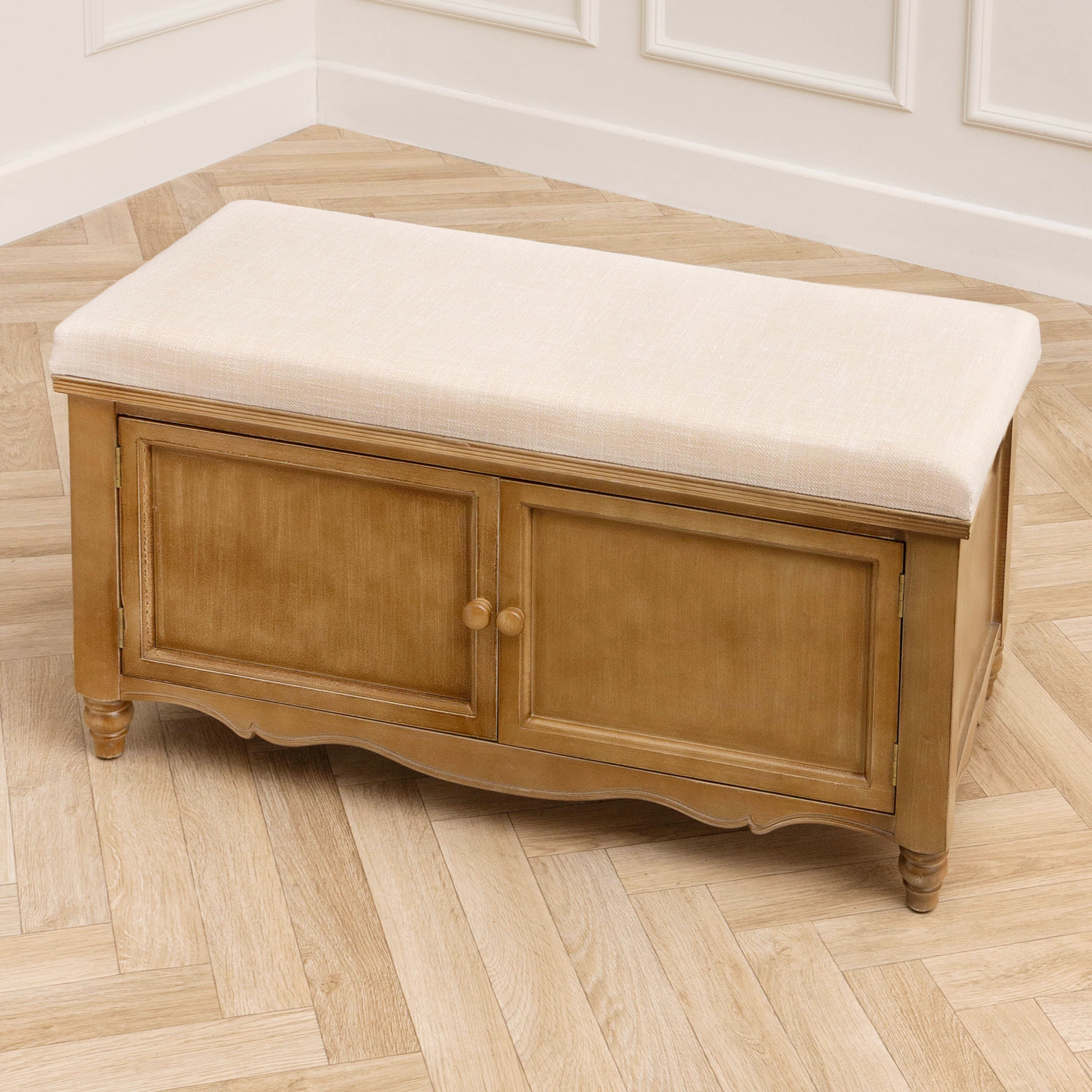 Rosalie oak finish storage bench with 2 doors and cream upholstered seat on a light wood floor with panelled walls.