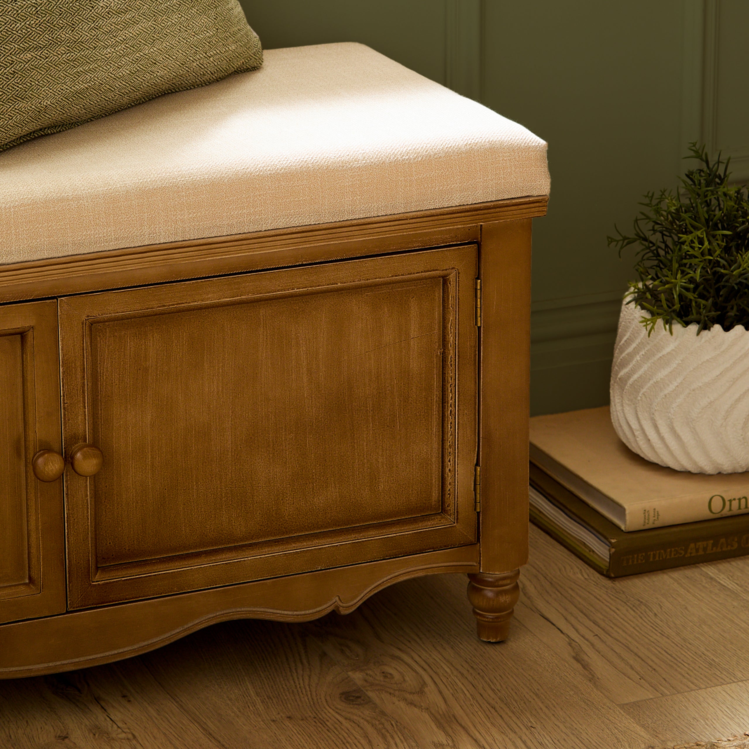 Close-up of Rosalie oak finish storage bench with 2 cabinet doors beside books and a plant on a wood floor.