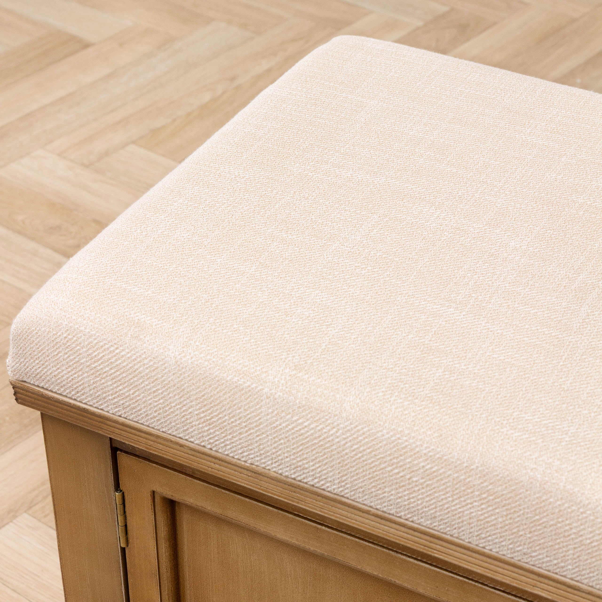 Close-up of Rosalie storage bench showing its cream upholstered seat and oak finish frame over herringbone flooring.