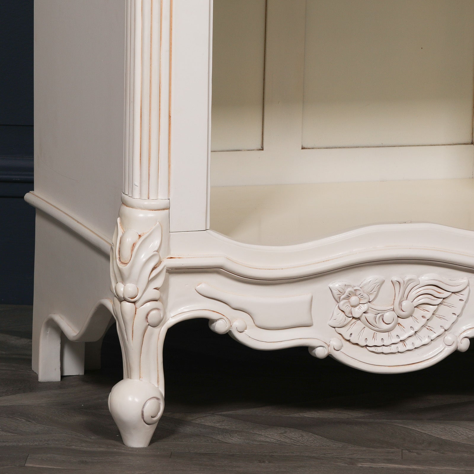 Detailed view of the Rosalie Tall French Open Bookcase highlighting the beautifully hand-carved apron, cabriole feet, fluted column, floral carvings and Antique White mahogany wood finish for timeless French luxury interiors.