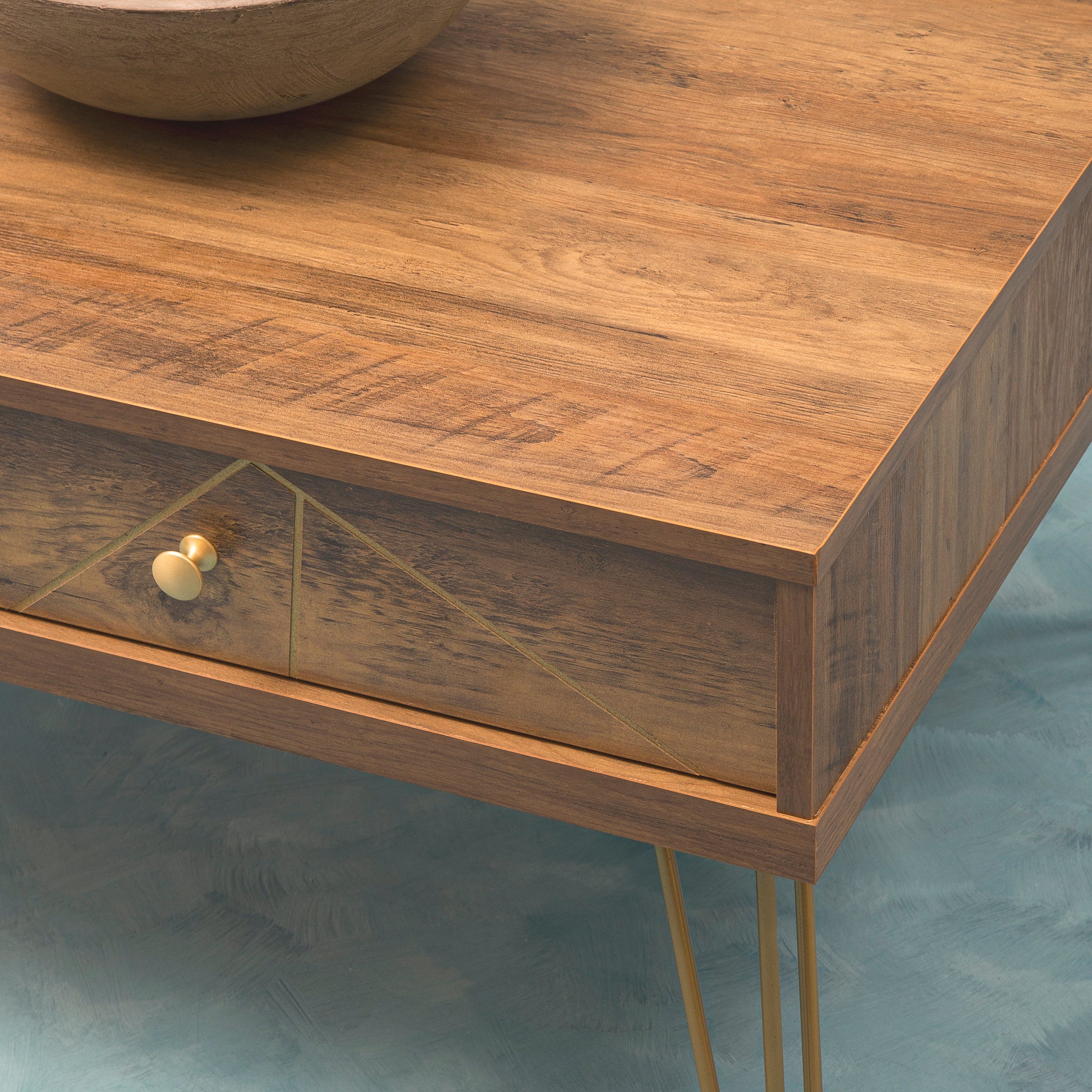 Close-up of the Soline Mid-Century Coffee Table showing its warm wood-effect top, geometric drawer front, round gold handle and slim gold metal hairpin legs.
