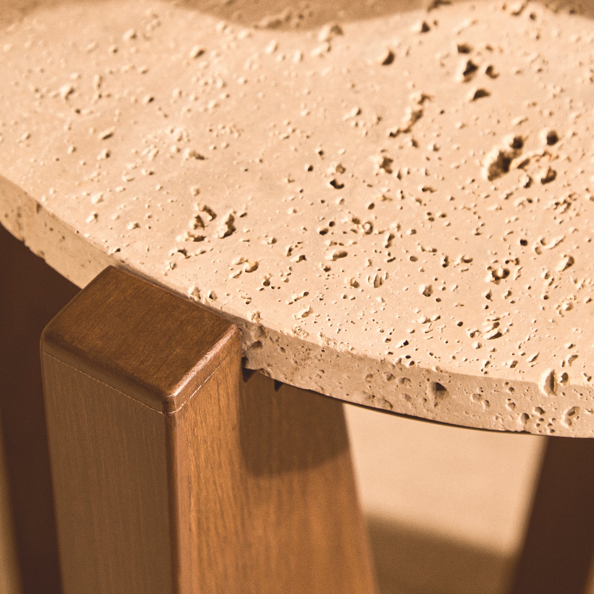 Close-up of the Soline Side Table showing the natural texture and porous detailing of its round travertine top beside the acacia wood frame