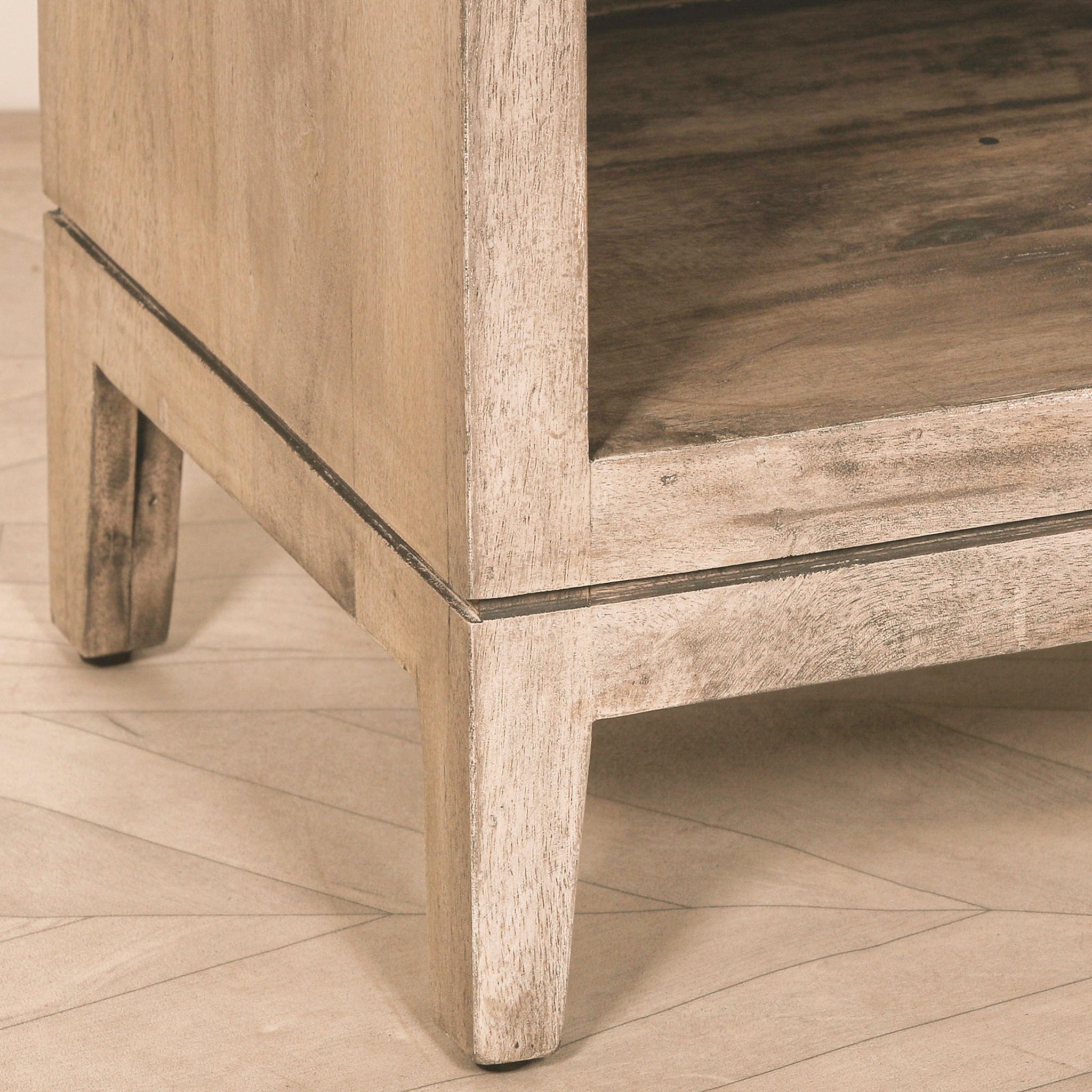 Close-up detail of the Soline rustic mango wood bedside table highlighting the handcrafted solid mango wood frame, natural wood grain, sturdy tapered legs and lower open shelf with rustic finish.