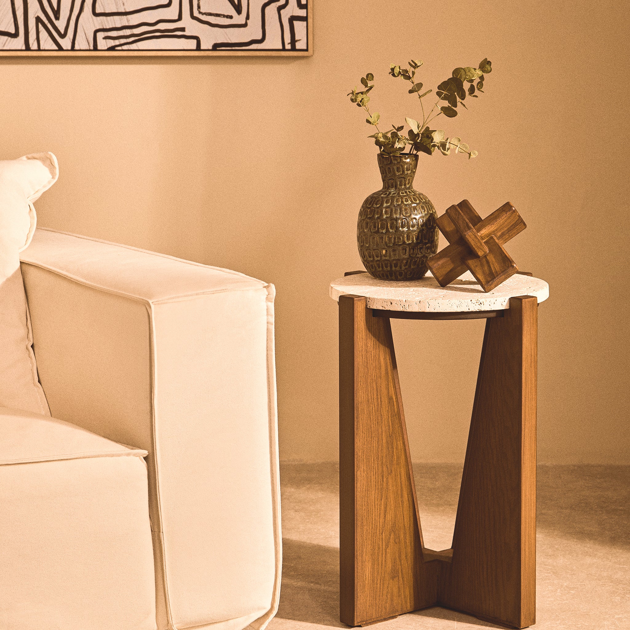 Soline Side Table with round travertine top and sculptural acacia wood frame styled beside a cream sofa with decorative vase and wooden ornament