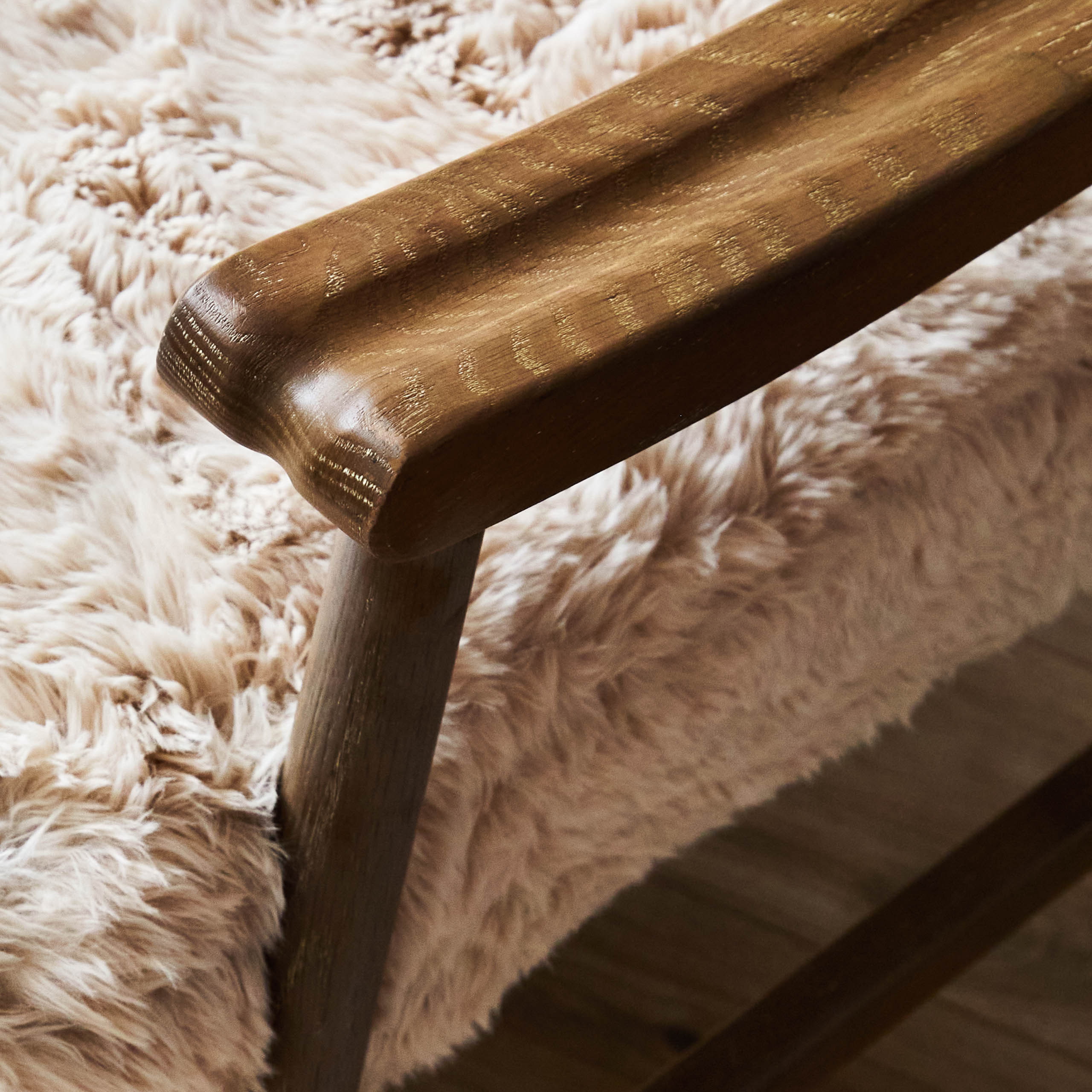 Close-up of Struan solid oak accent chair arm and natural upholstery with light wood flooring in background