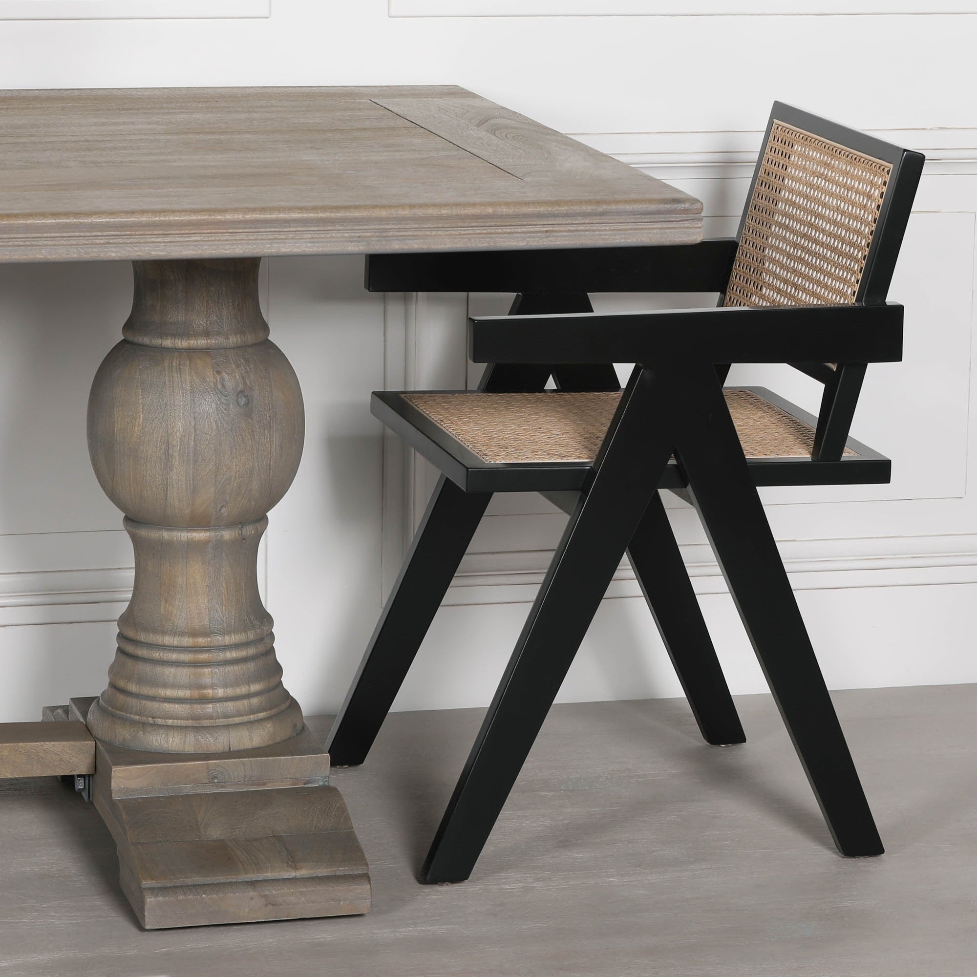 Close-up of the Théodore Large Rectangular Dining Table 240cm in Rustic Mango Wood with turned pedestal base alongside a black woven dining chair, showcasing premium solid wood craftsmanship and elegant contemporary styling.