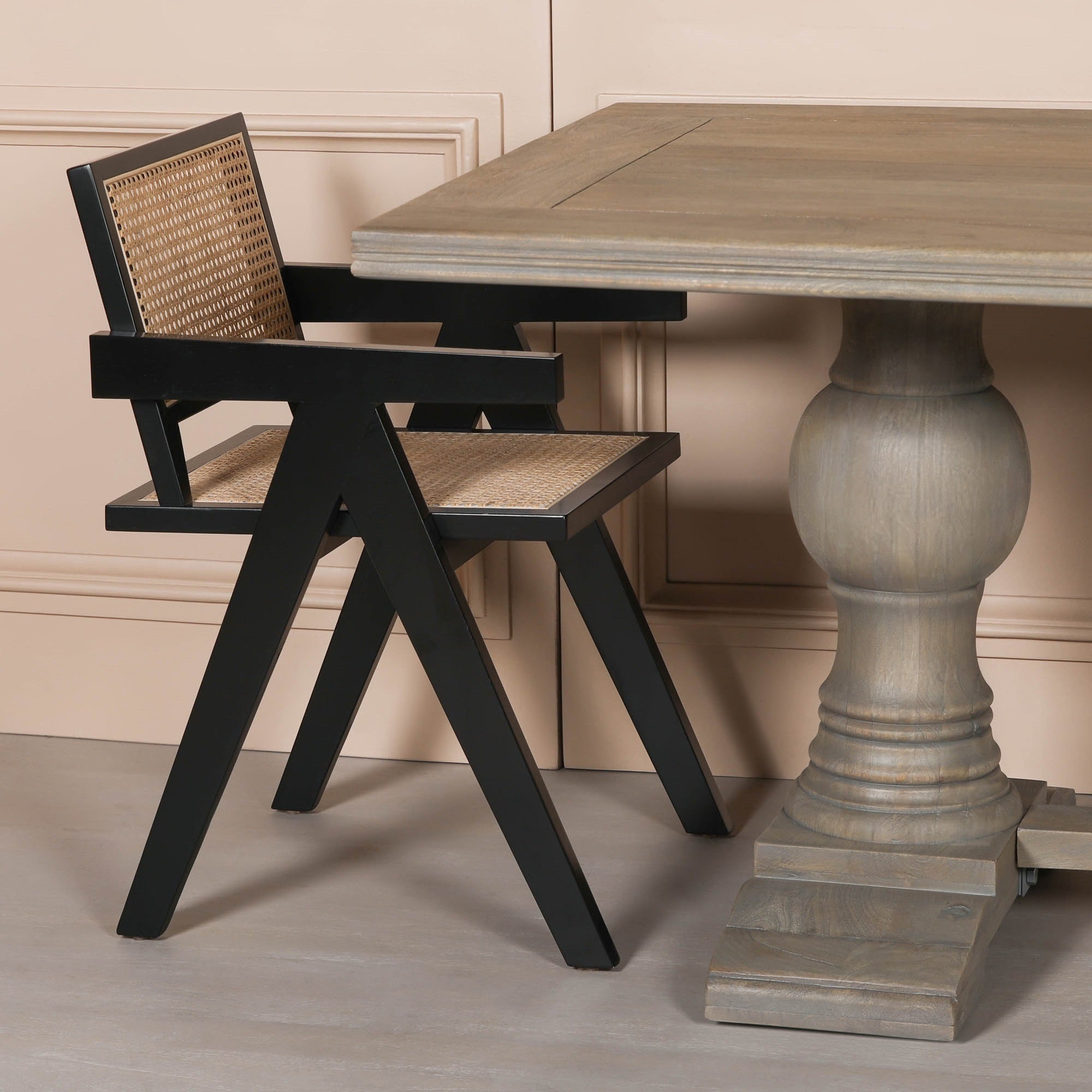 Théodore Large Rectangular Dining Table 240cm in Rustic Mango Wood paired with a black dining chair featuring a woven rattan backrest, showcasing the substantial pedestal base, thick tabletop and elegant contemporary dining room styling.