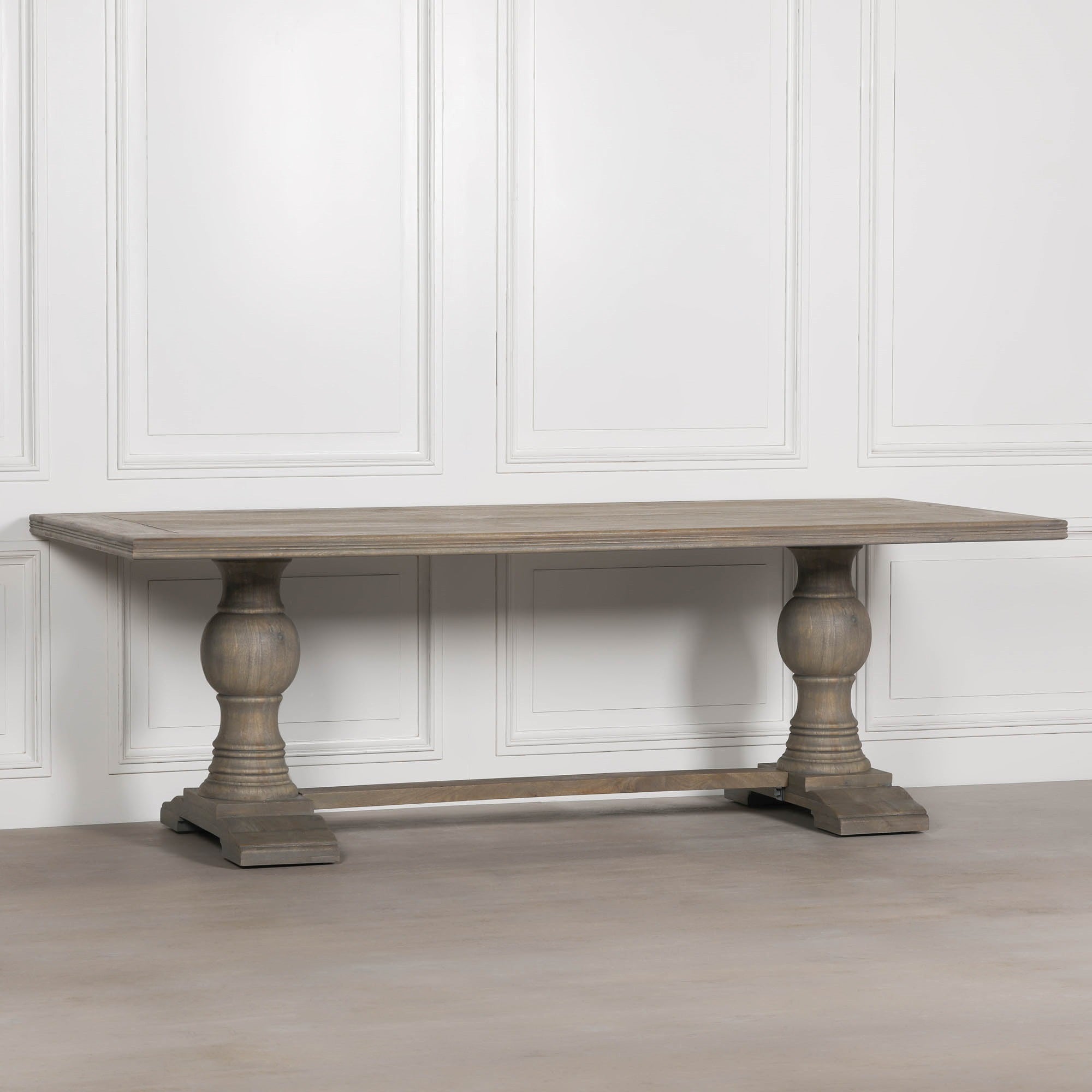 Three-quarter view of the Théodore Large Rectangular Dining Table 240cm for 10–12 in Rustic Mango Wood highlighting the expansive rectangular tabletop, sculptural pedestal legs, solid wood trestle base and timeless farmhouse-inspired design.