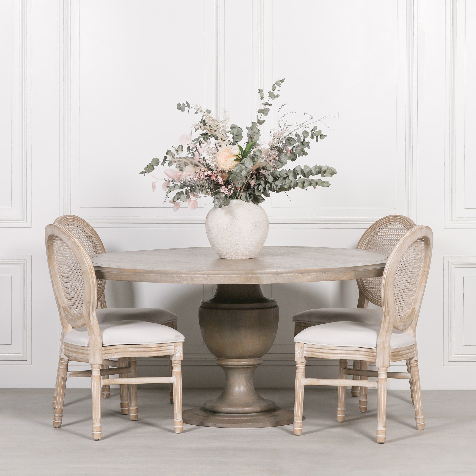 Théodore Large Round Dining Table 162cm for 6–8 in Rustic Mango Wood styled with upholstered rattan dining chairs and a floral centrepiece, showcasing the spacious solid mango wood tabletop, sculptural pedestal base and timeless rustic farmhouse dining room design for six to eight people.