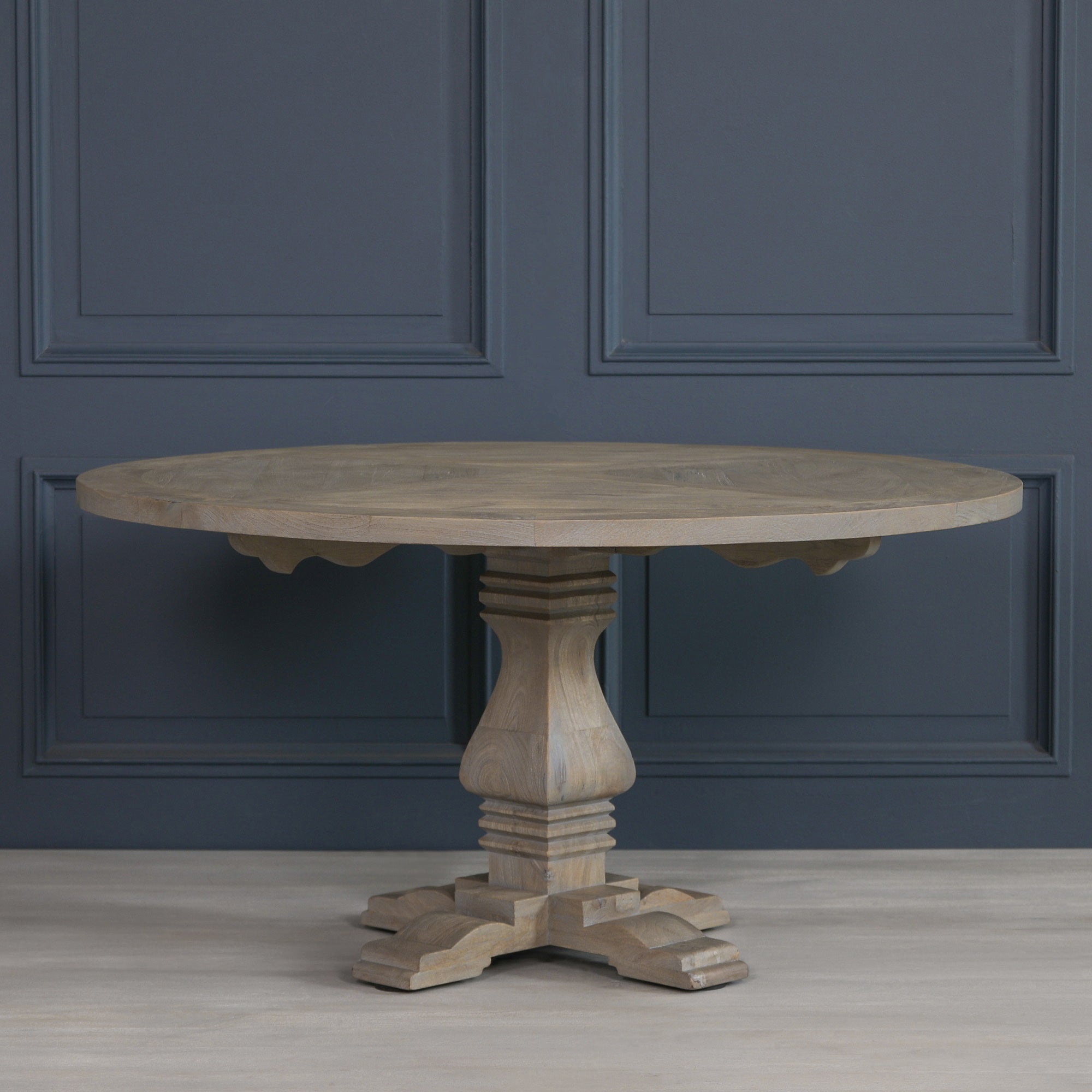 Théodore Round Pedestal Dining Table for 6 in Rustic White Cedar Style displayed against a dark interior backdrop, highlighting the spacious round tabletop, sculptural pedestal base, solid wood construction and elegant rustic farmhouse aesthetic.