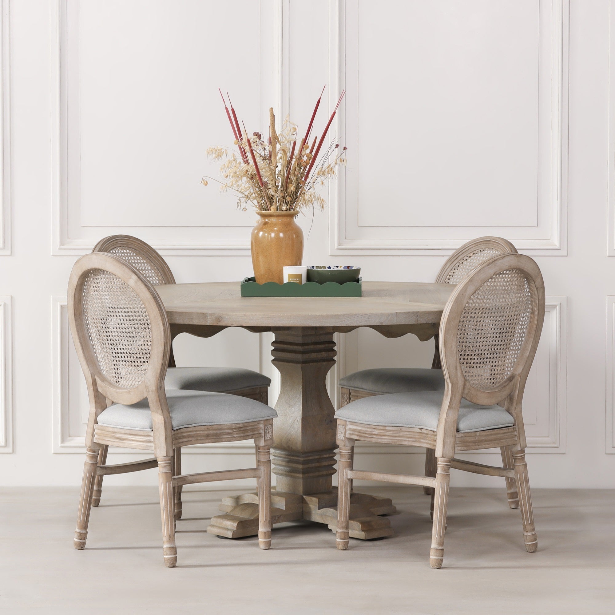 Théodore Round Pedestal Dining Table for 6 in Rustic White Cedar Style styled with upholstered rattan dining chairs in an elegant dining room, showcasing the solid wood round tabletop, sculptural pedestal base, rustic finish and spacious design for comfortable seating for six people.