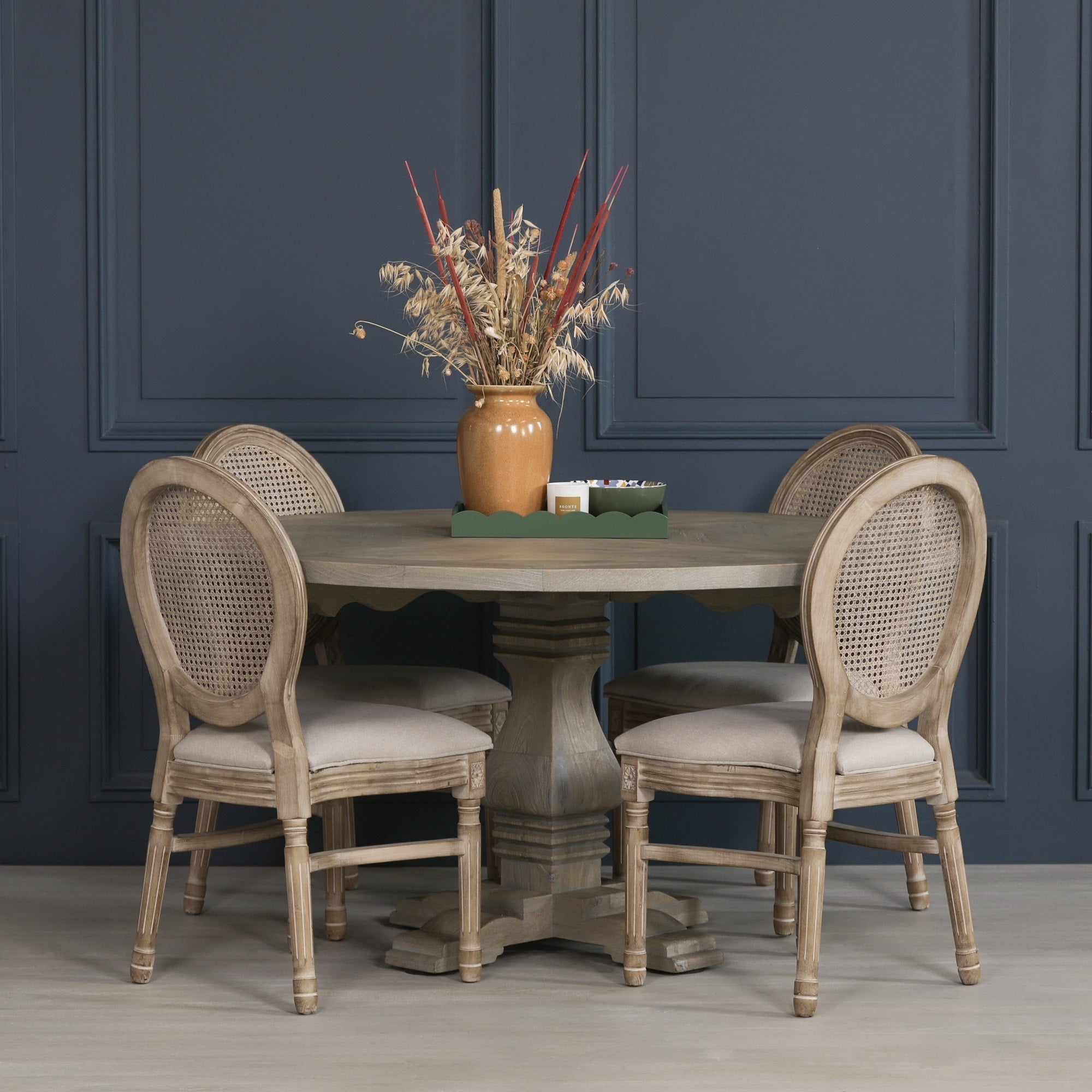 Théodore Round Pedestal Dining Table for 6 in Rustic White Cedar Style styled with upholstered rattan dining chairs, demonstrating the generous round tabletop, handcrafted pedestal base, rustic wood finish and inviting dining space for six people.