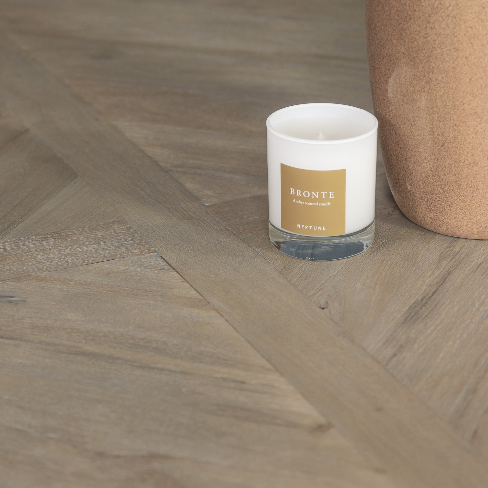 Close-up of the Théodore Round Pedestal Dining Table tabletop showcasing the natural wood grain, rustic white cedar style finish, parquet-inspired surface detailing and durable handcrafted construction for everyday dining. with a bronte candle showcased on the surface.