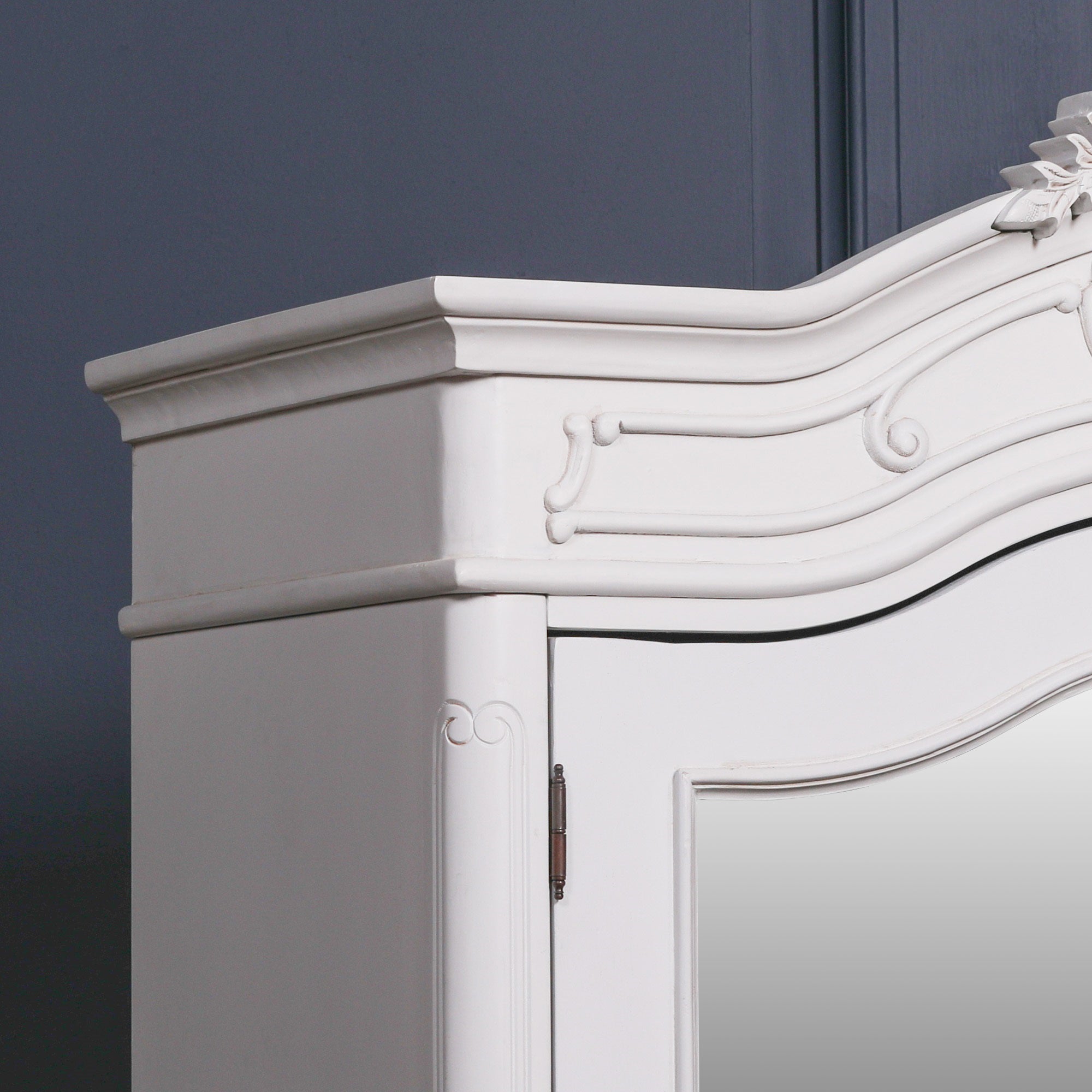Close-up of the Vivienne White Carved Mirrored Double Door Armoire Wardrobe showcasing the sculpted cornice, decorative mouldings, painted white finish, mirrored door frame and handcrafted French-inspired detailing.